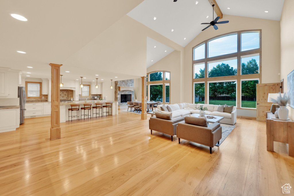 Living room with high vaulted ceiling, light wood-type flooring, a ceiling fan, a fireplace, and beamed ceiling