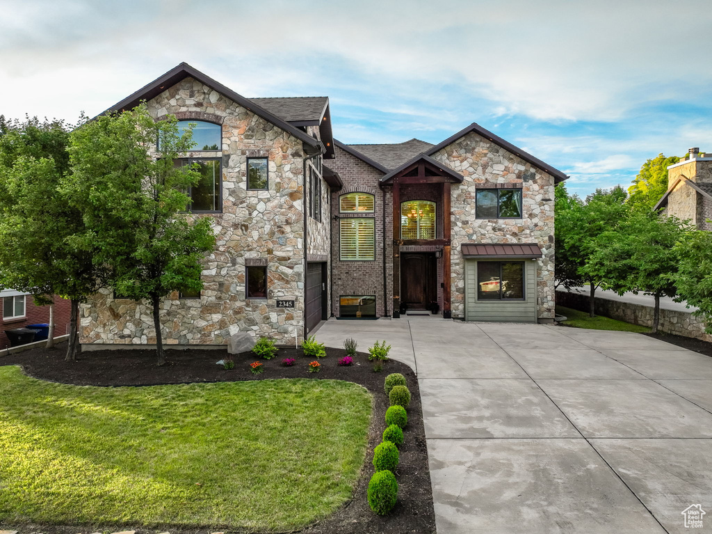 French country style house with stone siding, a front lawn, driveway, and an attached garage