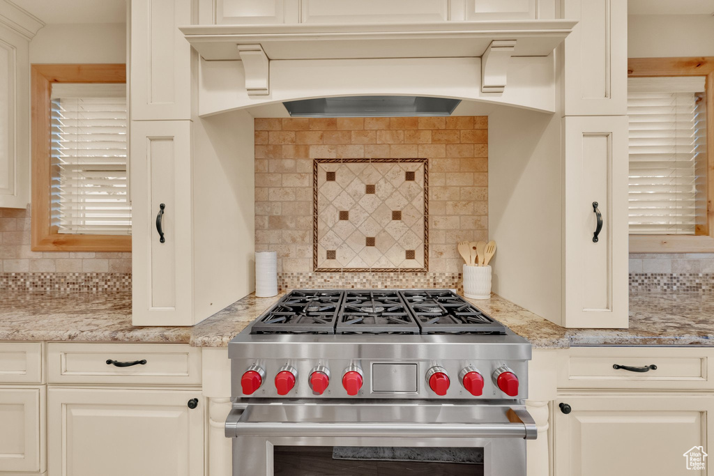 Kitchen featuring high end stainless steel range, tasteful backsplash, light stone counters, and custom exhaust hood