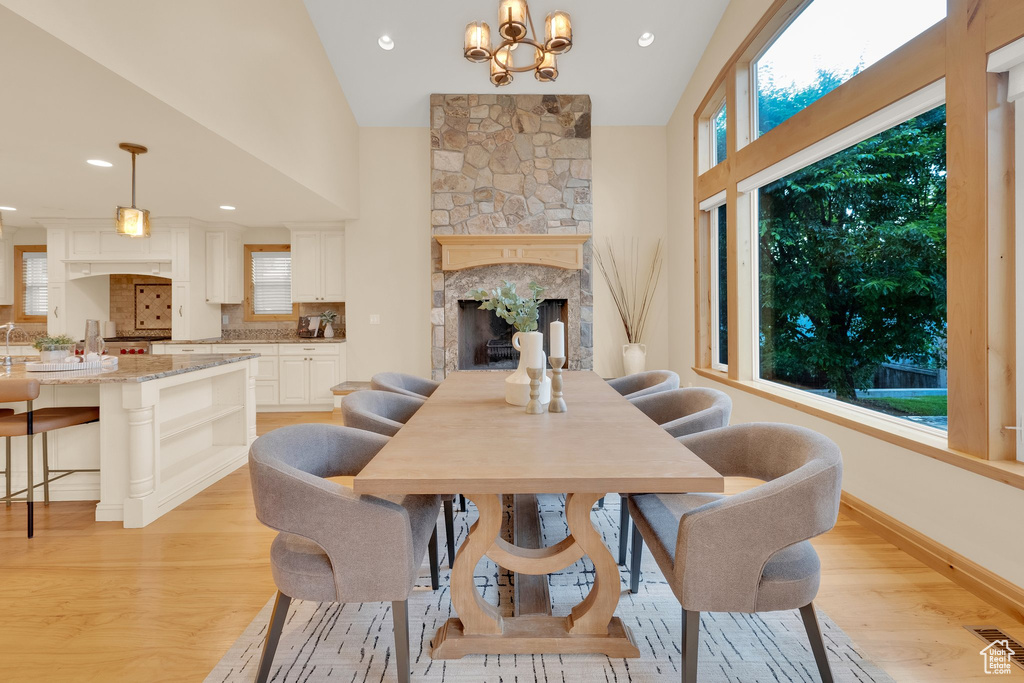 Dining area featuring light wood-style flooring, a fireplace, healthy amount of natural light, high vaulted ceiling, and baseboards