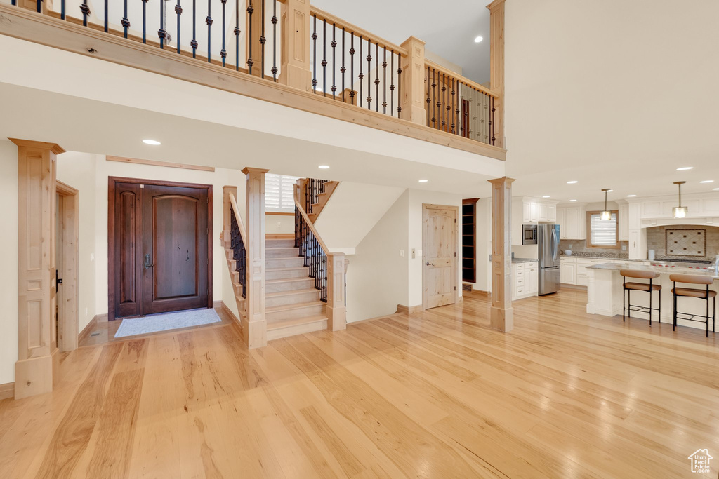 Foyer featuring light wood-style flooring, stairs, recessed lighting, decorative columns, and a towering ceiling