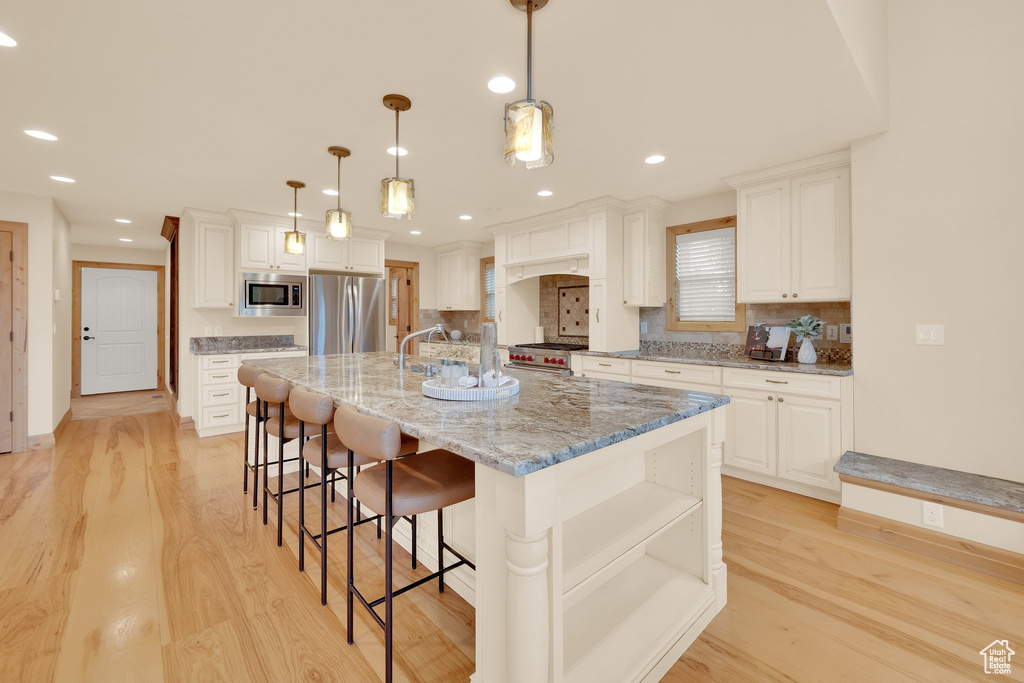 Kitchen featuring appliances with stainless steel finishes, light wood finished floors, decorative backsplash, a breakfast bar, and recessed lighting