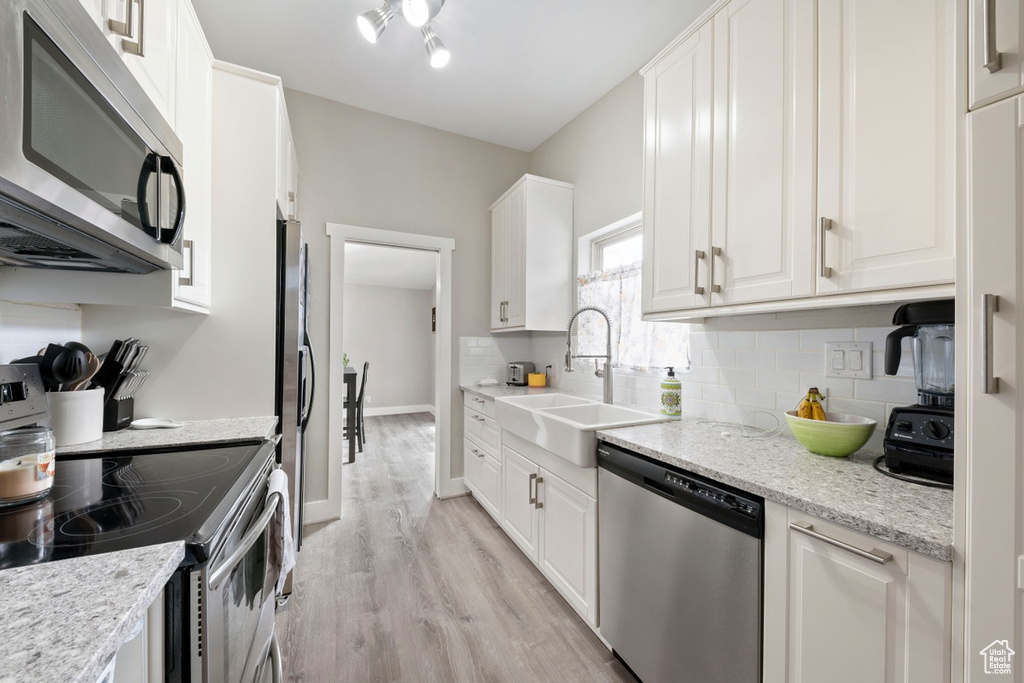 Kitchen featuring stainless steel appliances, a sink, light wood-style floors, and white cabinetry