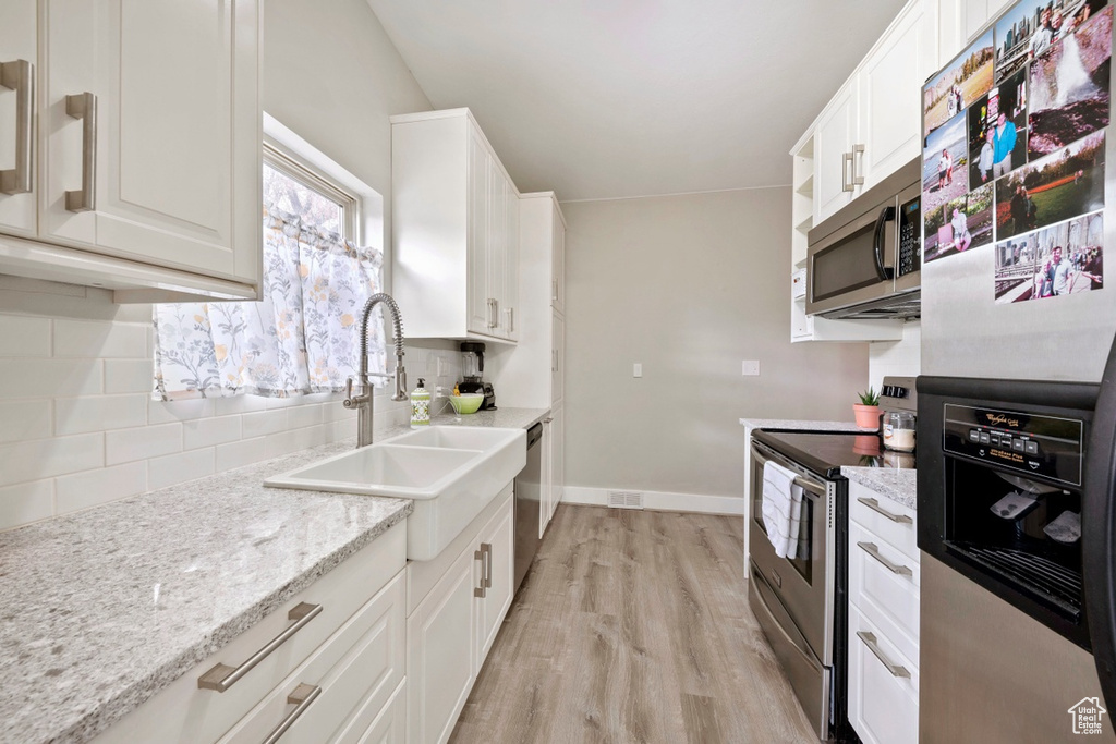 Kitchen featuring appliances with stainless steel finishes, decorative backsplash, a sink, light wood finished floors, and white cabinetry