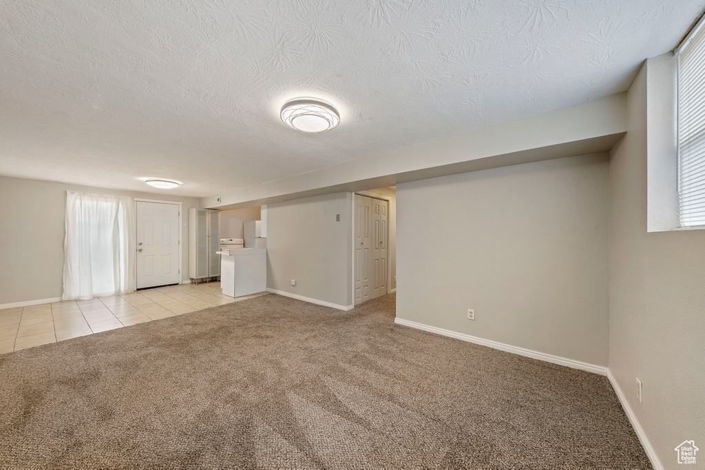 Empty room with light carpet, baseboards, a textured ceiling, and light tile patterned flooring