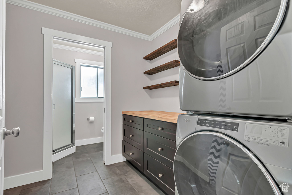Washroom featuring stacked washer / drying machine, cabinet space, ornamental molding, baseboards, and dark tile patterned floors