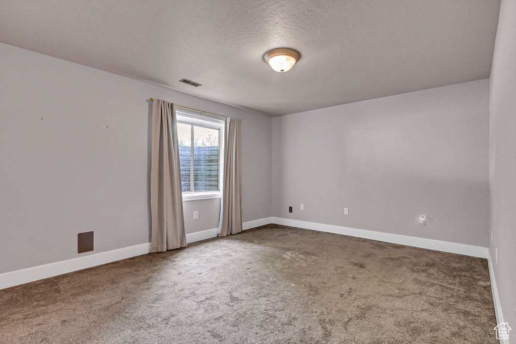 Empty room with carpet flooring, baseboards, and a textured ceiling