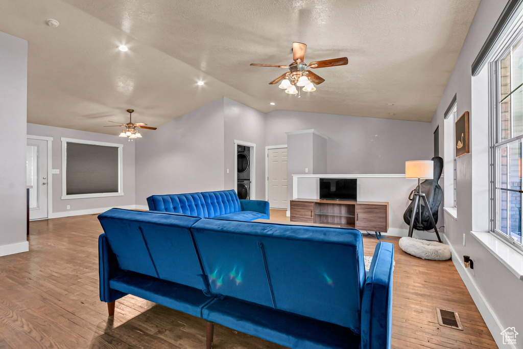 Living room with stacked washer / drying machine, ceiling fan, wood finished floors, healthy amount of natural light, and a textured ceiling