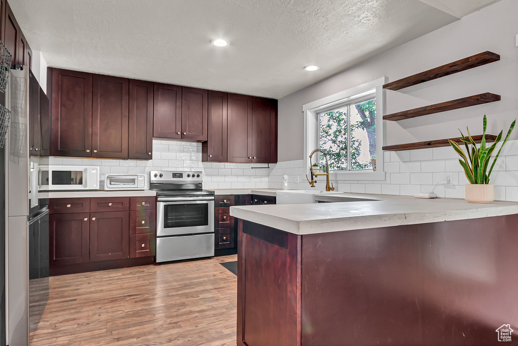 Kitchen with stainless steel range with electric stovetop, open shelves, a peninsula, a sink, and white microwave