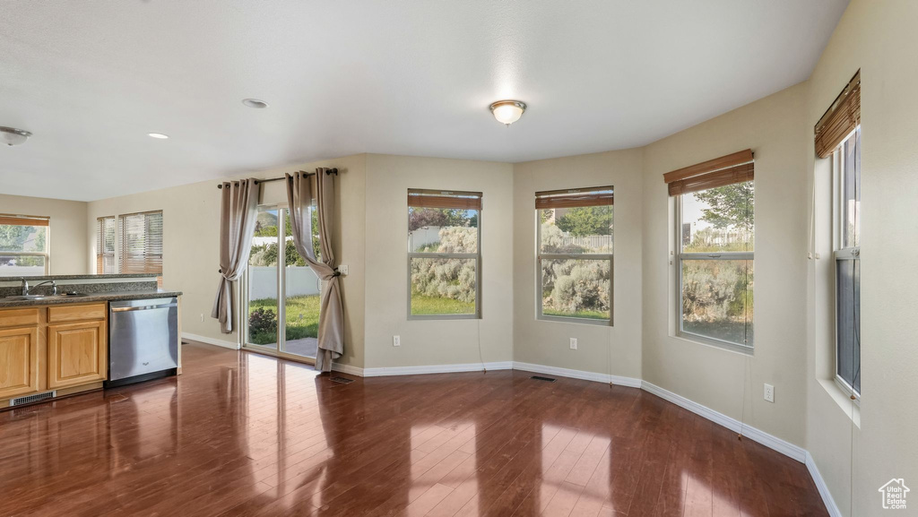 Kitchen with stainless steel dishwasher, dark countertops, dark wood-style floors, baseboards, and plenty of natural light