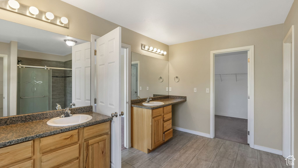 Bathroom with a stall shower, two vanities, a spacious closet, baseboards, and wood tiled floors