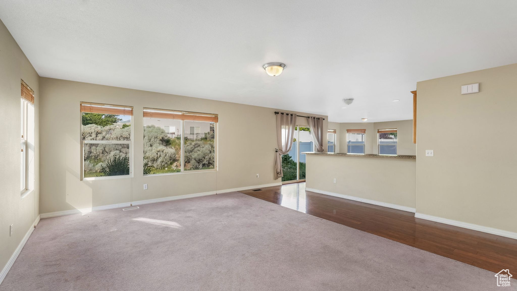 Unfurnished living room with healthy amount of natural light, baseboards, carpet, and wood finished floors