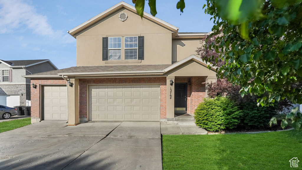 Traditional-style house with brick siding, driveway, a garage, a front yard, and stucco siding