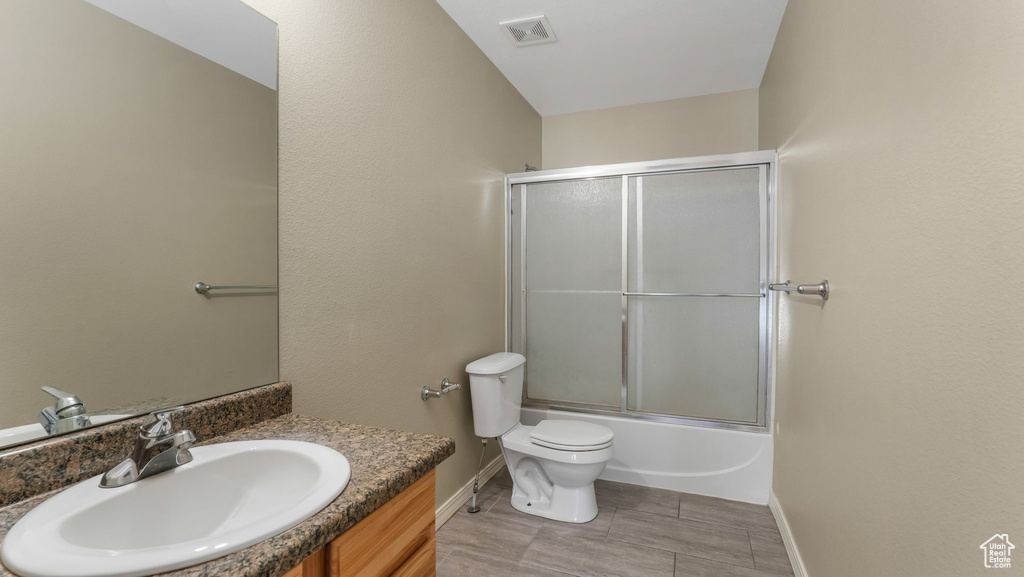 Full bathroom with baseboards, toilet, vanity, and bath / shower combo with glass door