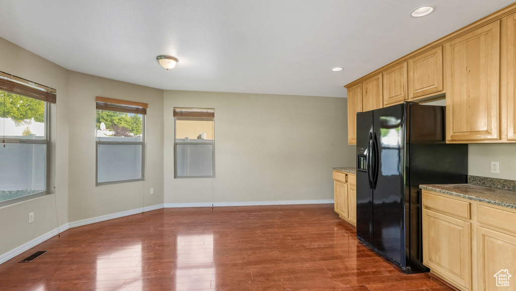 Kitchen featuring black refrigerator with ice dispenser, dark wood-style floors, recessed lighting, baseboards, and stone countertops
