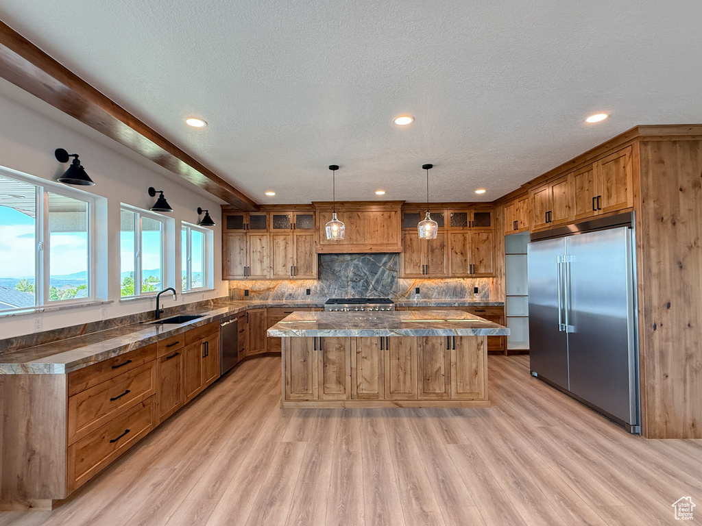 Kitchen featuring stainless steel appliances, a center island, a sink, brown cabinets, and light wood finished floors