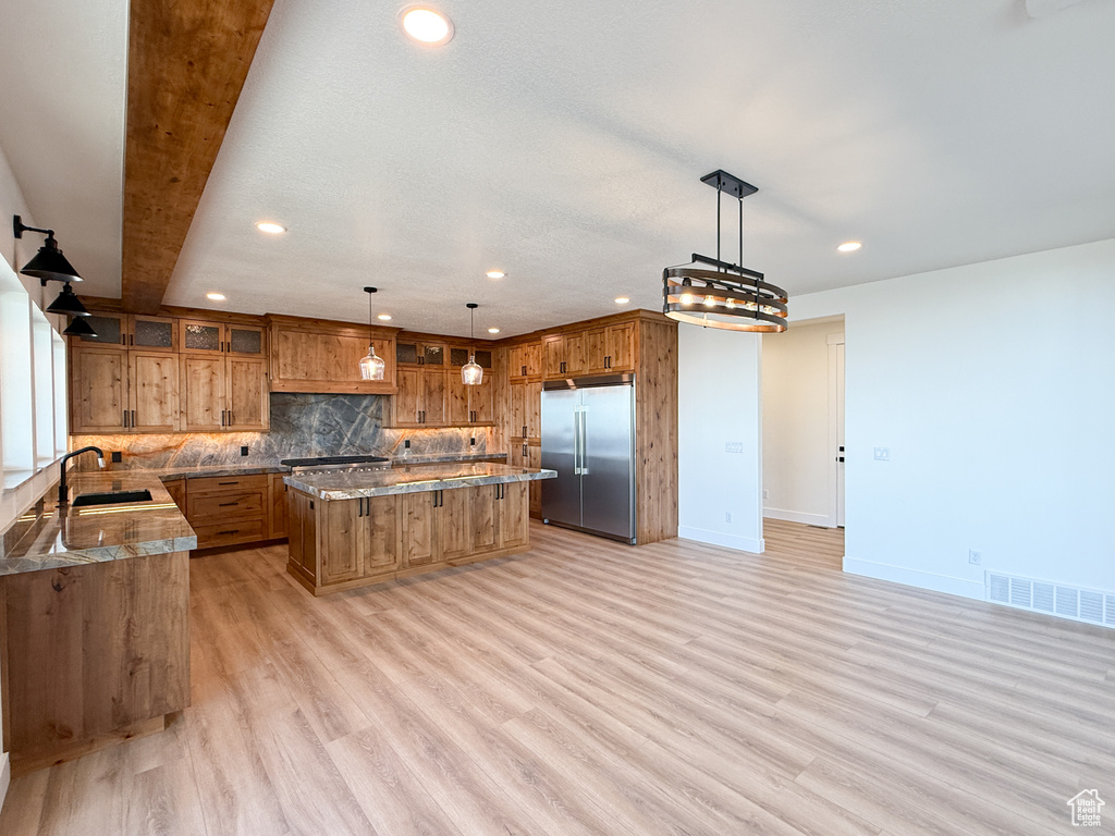 Kitchen featuring built in refrigerator, brown cabinetry, a sink, recessed lighting, and a center island