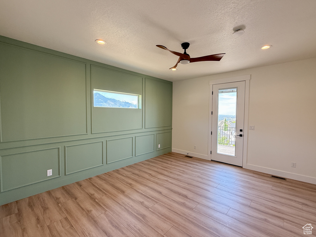 Unfurnished room with a decorative wall, baseboards, light wood finished floors, a textured ceiling, and ceiling fan