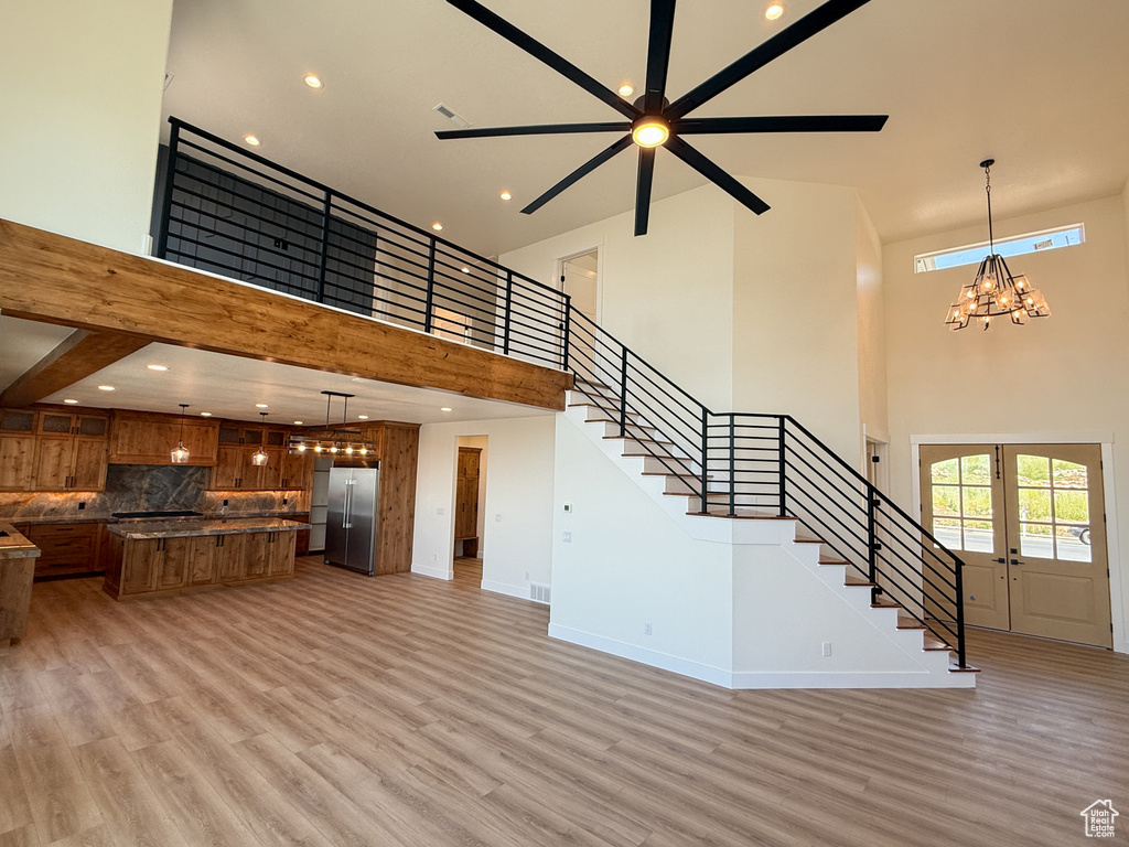 Unfurnished living room featuring a high ceiling, stairway, light wood-style flooring, baseboards, and a ceiling fan