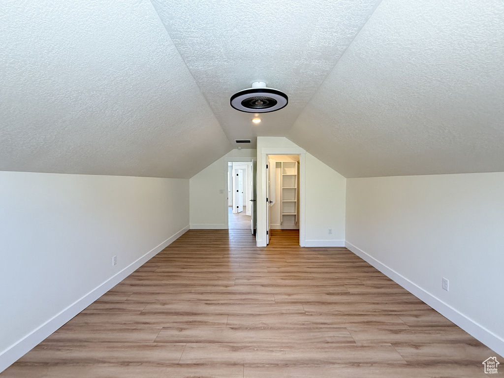 Additional living space featuring a textured ceiling, baseboards, light wood-type flooring, and vaulted ceiling