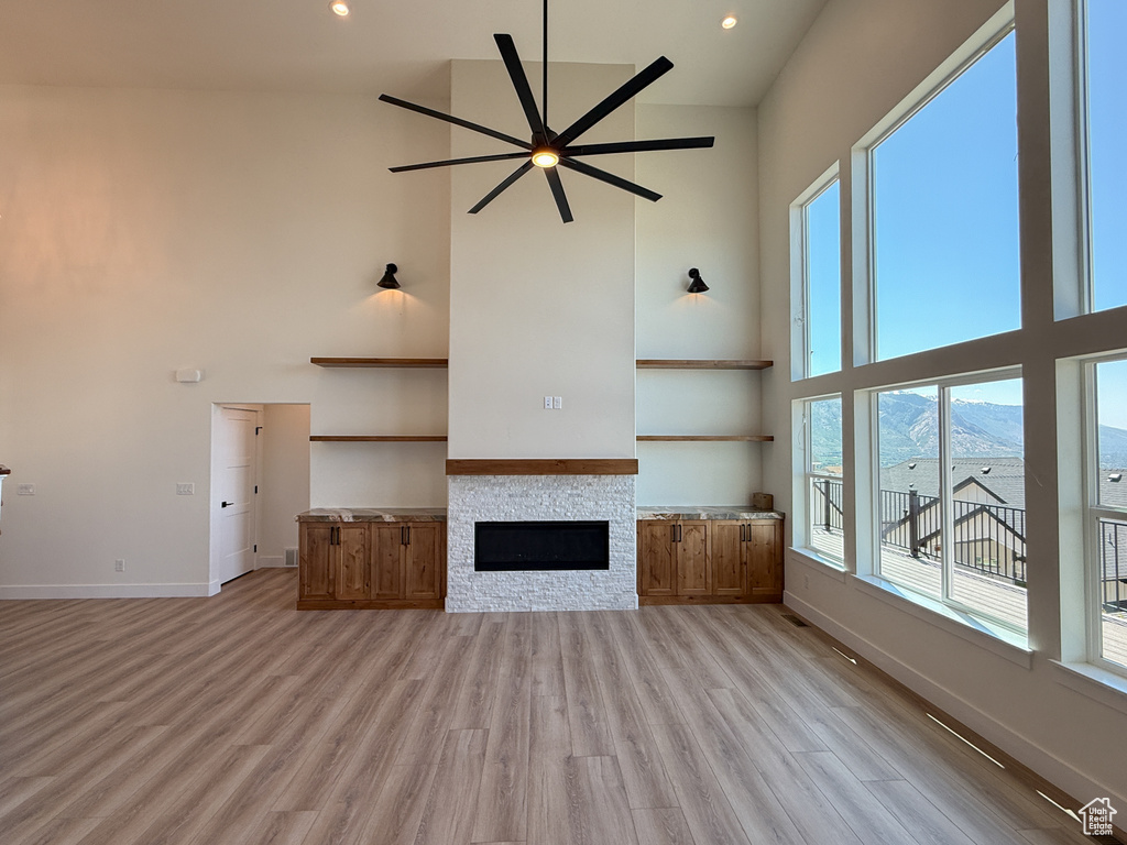 Unfurnished living room with a high ceiling, ceiling fan, light wood-style floors, baseboards, and a stone fireplace