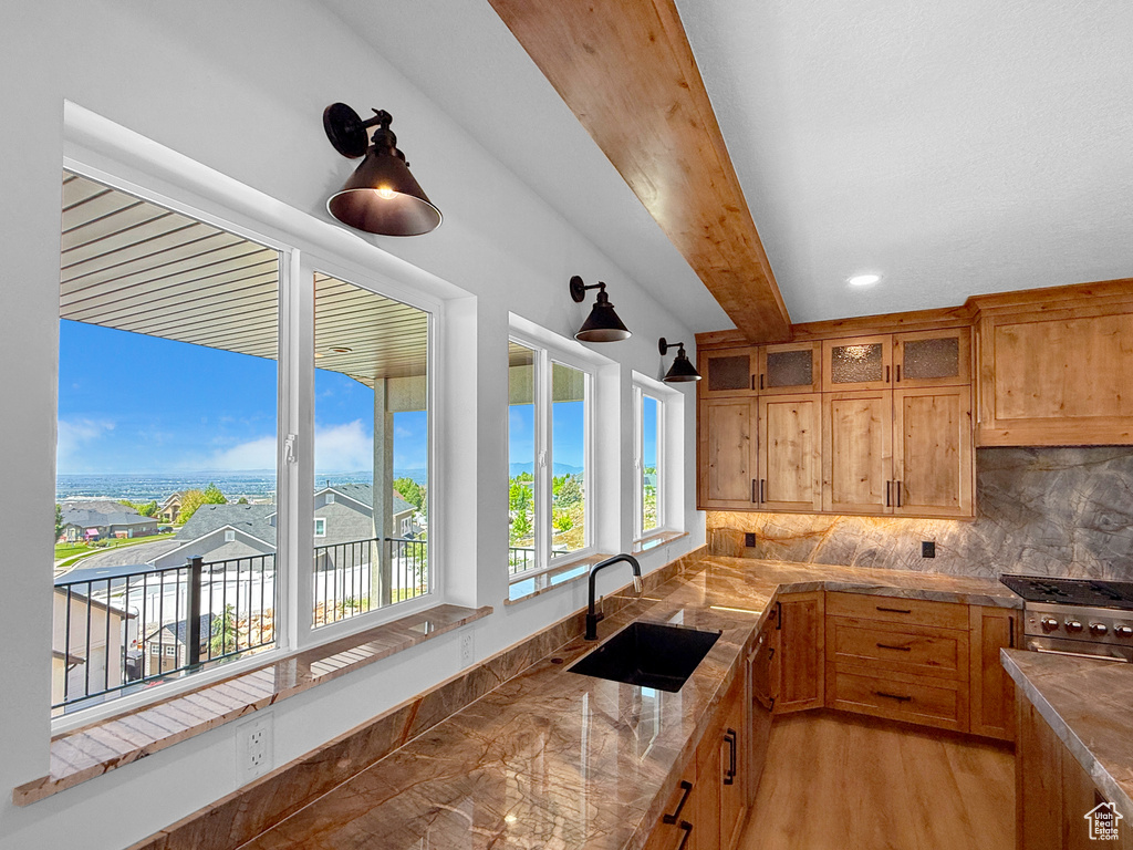 Kitchen featuring a sink, backsplash, glass insert cabinets, light wood finished floors, and light stone counters