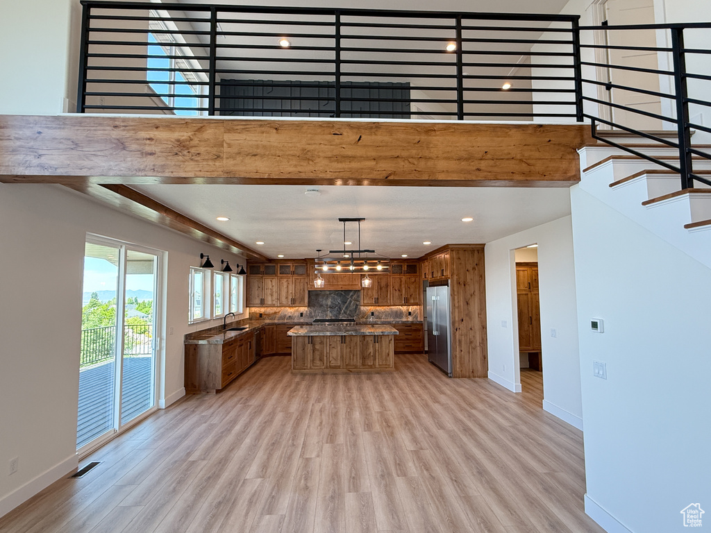 Kitchen with high quality fridge, brown cabinets, light wood-style flooring, tasteful backsplash, and recessed lighting