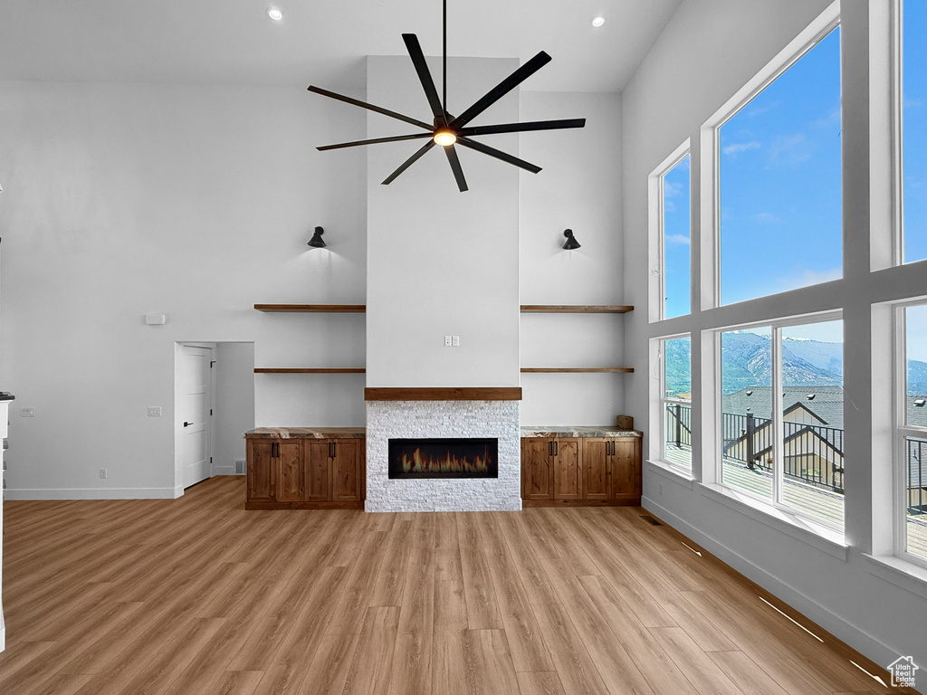 Unfurnished living room featuring a high ceiling, a ceiling fan, a stone fireplace, baseboards, and light wood-type flooring