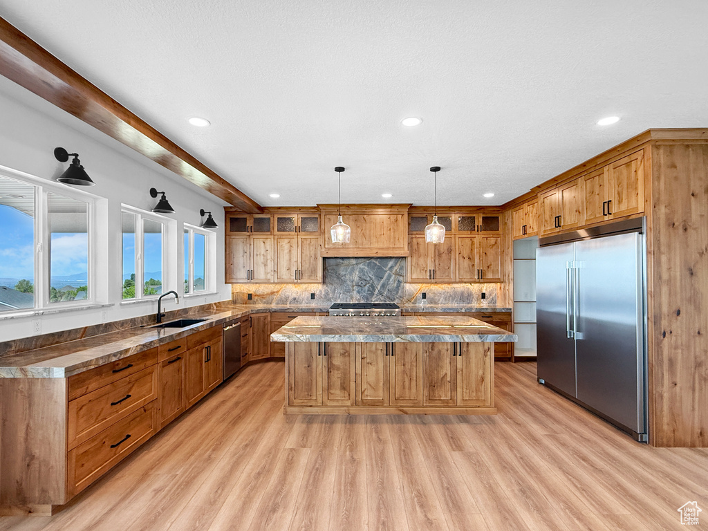 Kitchen with stainless steel appliances, a kitchen island, a sink, light wood finished floors, and glass insert cabinets