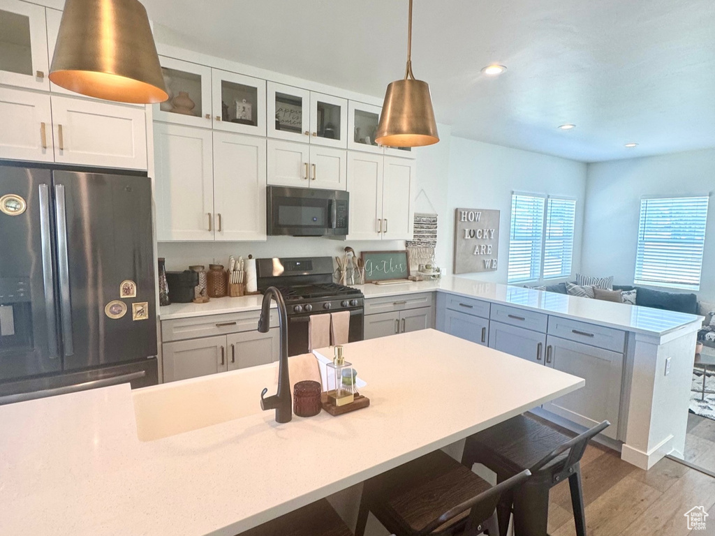 Kitchen with black appliances, a peninsula, wood finished floors, light countertops, and glass insert cabinets