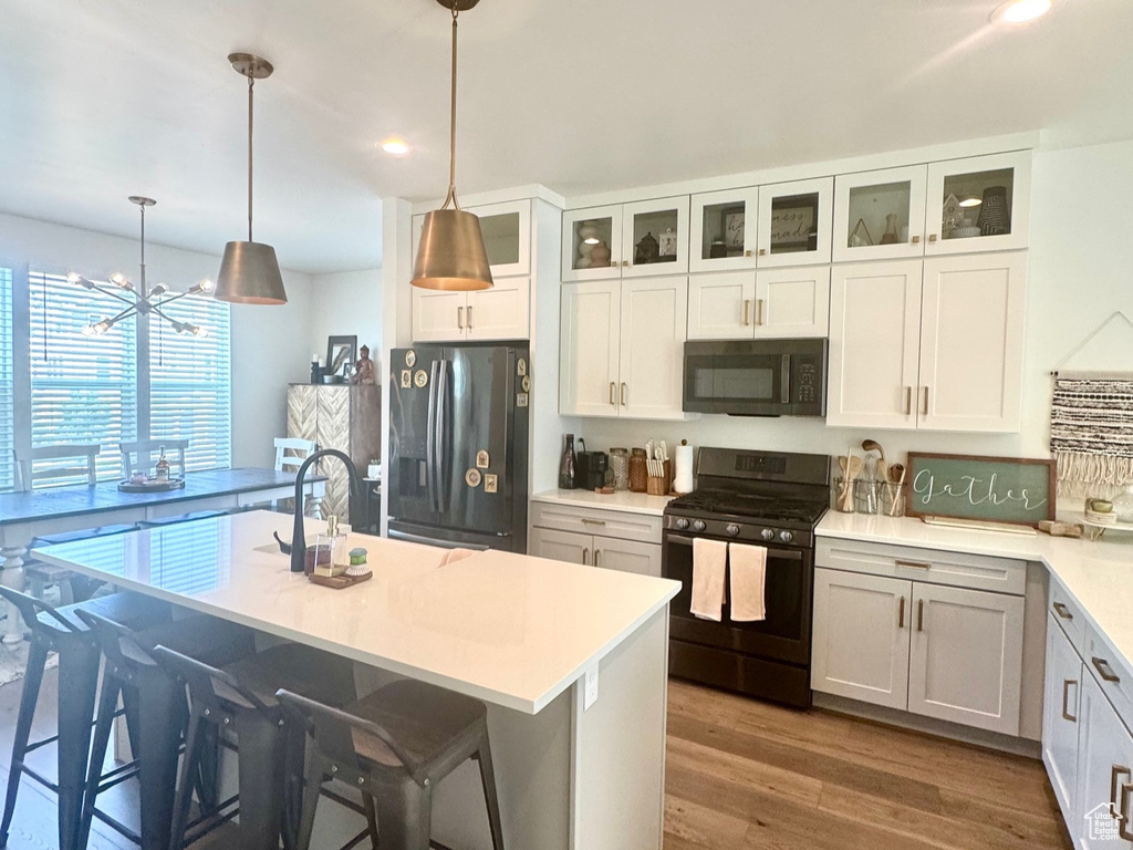 Kitchen featuring black appliances, wood finished floors, light countertops, glass insert cabinets, and white cabinetry