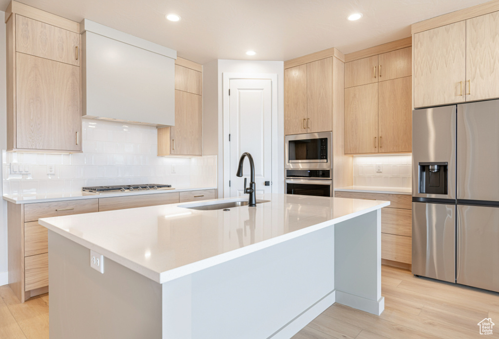 Kitchen with appliances with stainless steel finishes, a sink, light brown cabinets, light wood finished floors, and recessed lighting