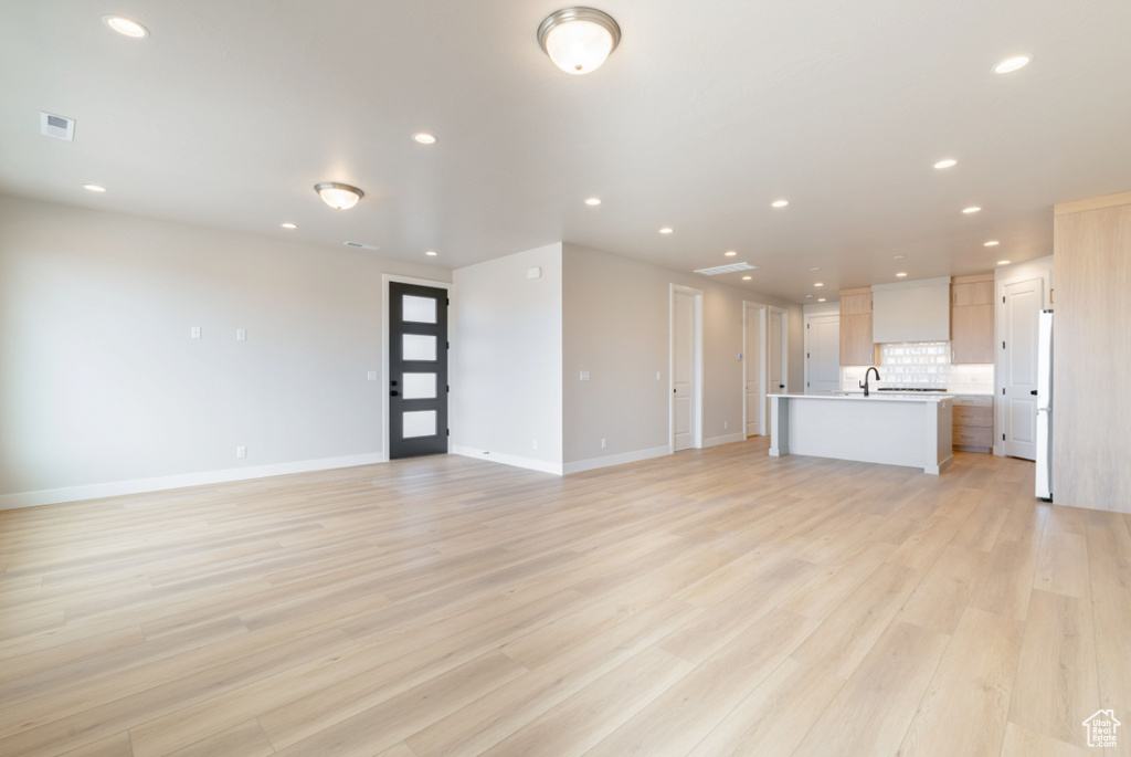 Unfurnished living room with recessed lighting, baseboards, light wood-style flooring, and a sink