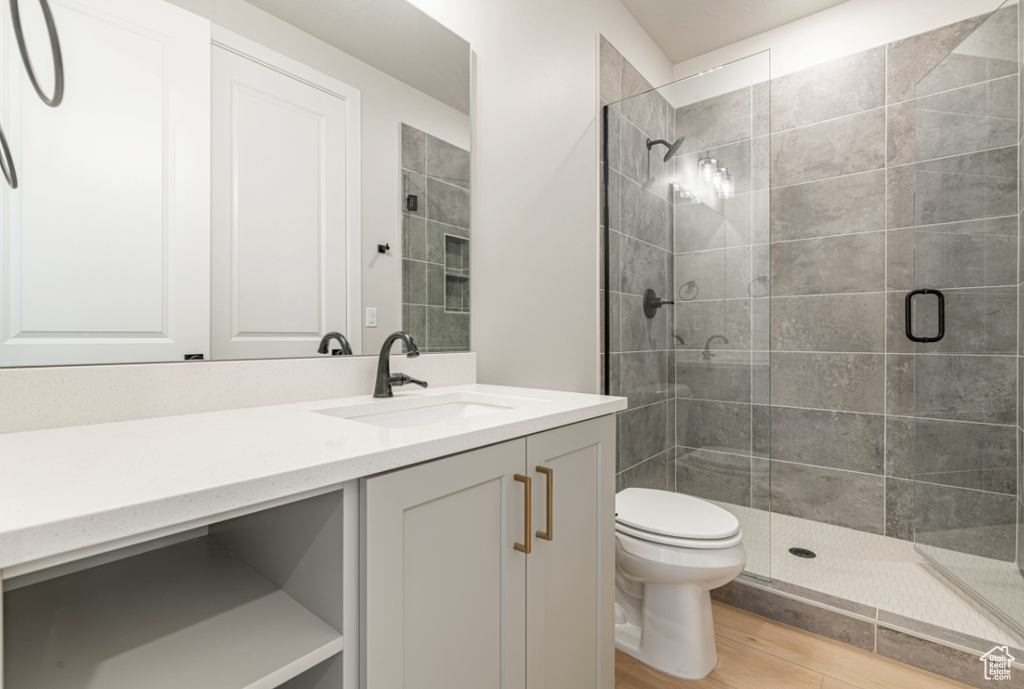 Full bath with toilet, a stall shower, vanity, and wood finished floors