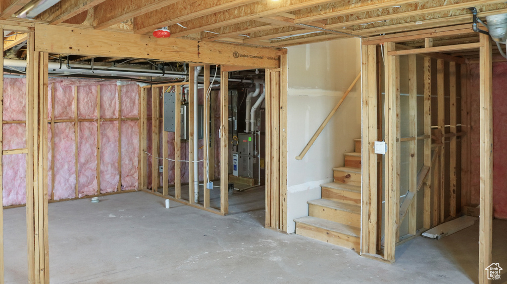 Unfinished basement featuring heating unit and stairs