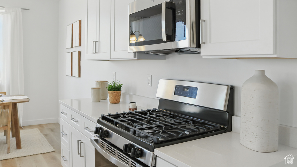 Kitchen featuring stainless steel appliances, white cabinetry, light countertops, light wood-style flooring, and baseboards