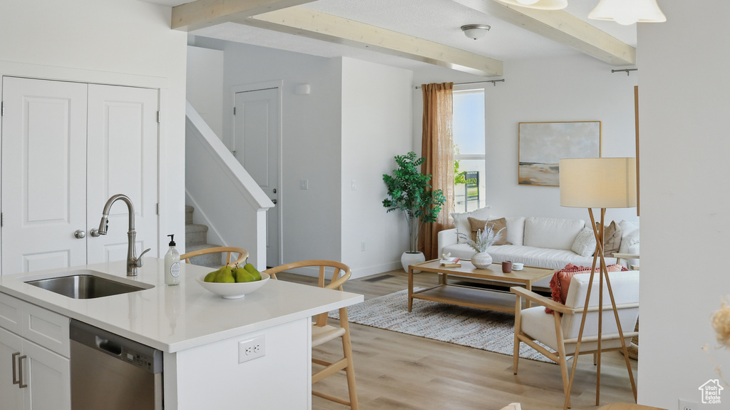 Kitchen featuring a sink, stainless steel dishwasher, beam ceiling, light wood-style flooring, and light countertops