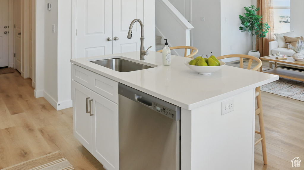 Kitchen featuring dishwasher, a sink, light wood finished floors, and a kitchen island with sink