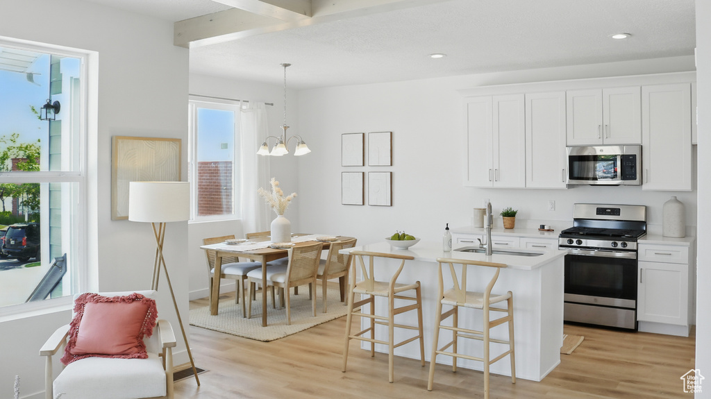 Kitchen featuring appliances with stainless steel finishes, a sink, light wood-style floors, light countertops, and a chandelier