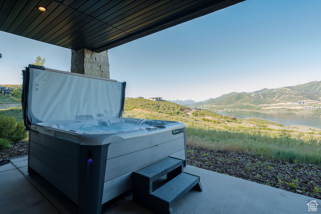 View of patio with a hot tub and a water and mountain view