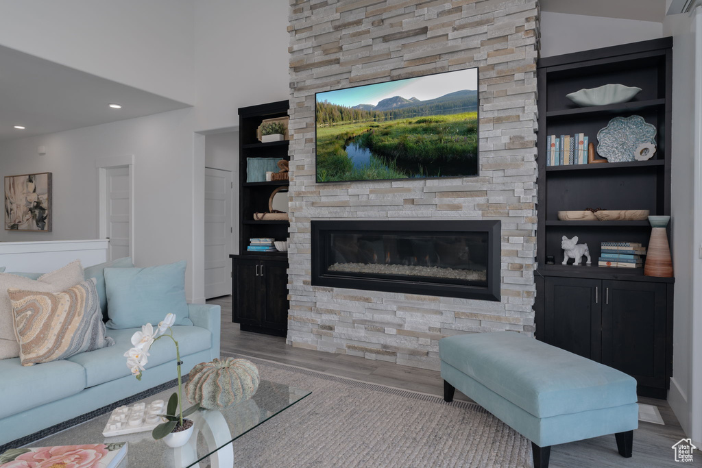 Living room with wood finished floors, a stone fireplace, built in shelves, and recessed lighting