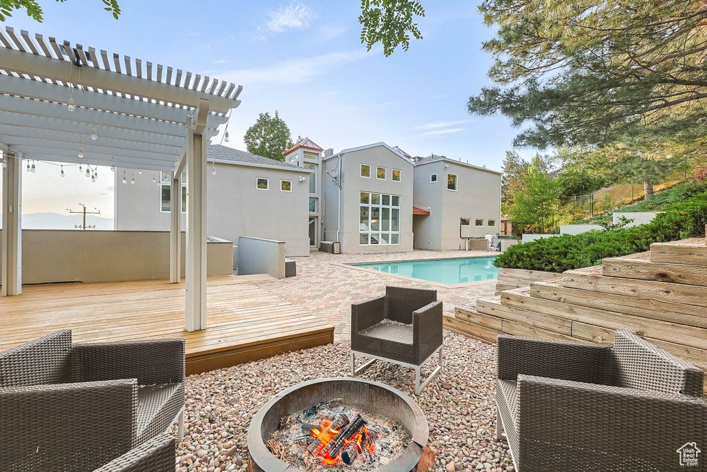 Outdoor pool with a fire pit, a wooden deck, and a pergola