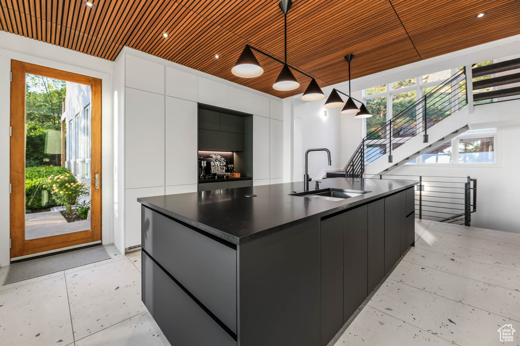 Kitchen with a sink, modern cabinets, dark countertops, wooden ceiling, and a kitchen island with sink