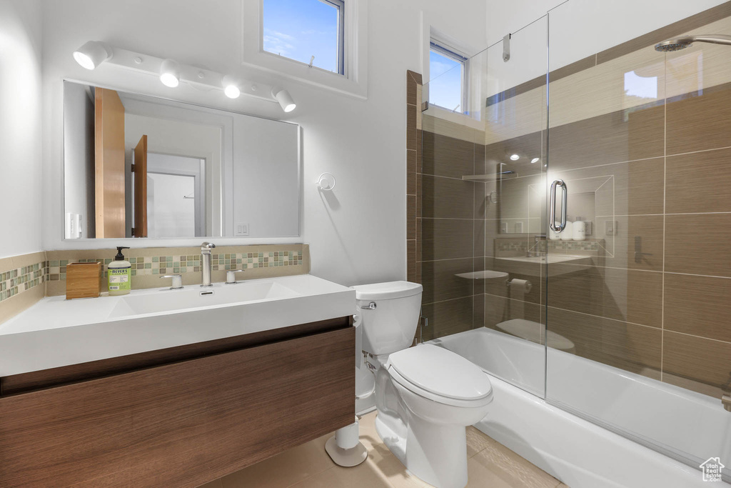 Bathroom with toilet, vanity, decorative backsplash, and bath / shower combo with glass door
