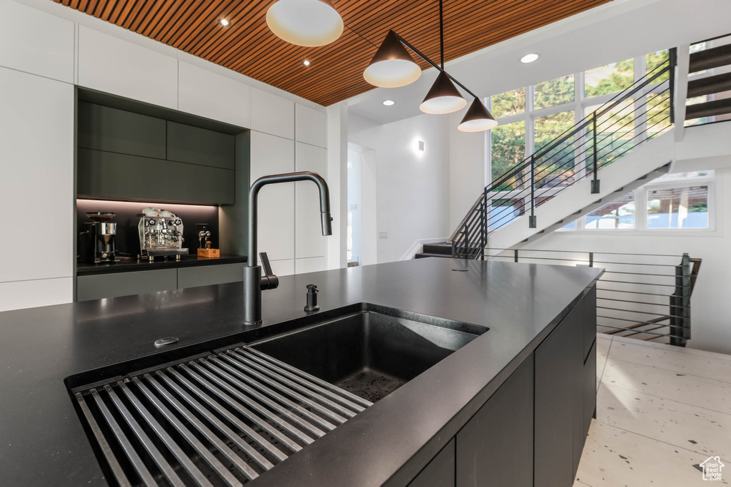 Kitchen with dark countertops, a sink, white cabinetry, and hanging light fixtures