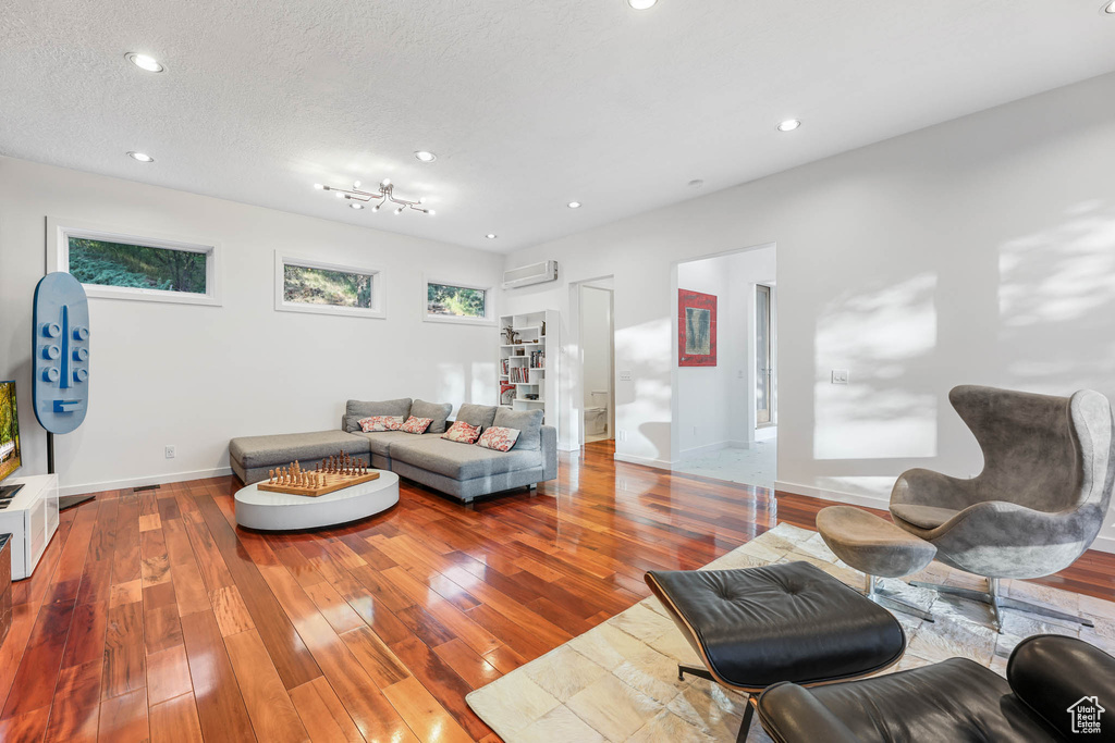 Living room featuring a wall mounted air conditioner, baseboards, hardwood / wood-style floors, recessed lighting, and a textured ceiling