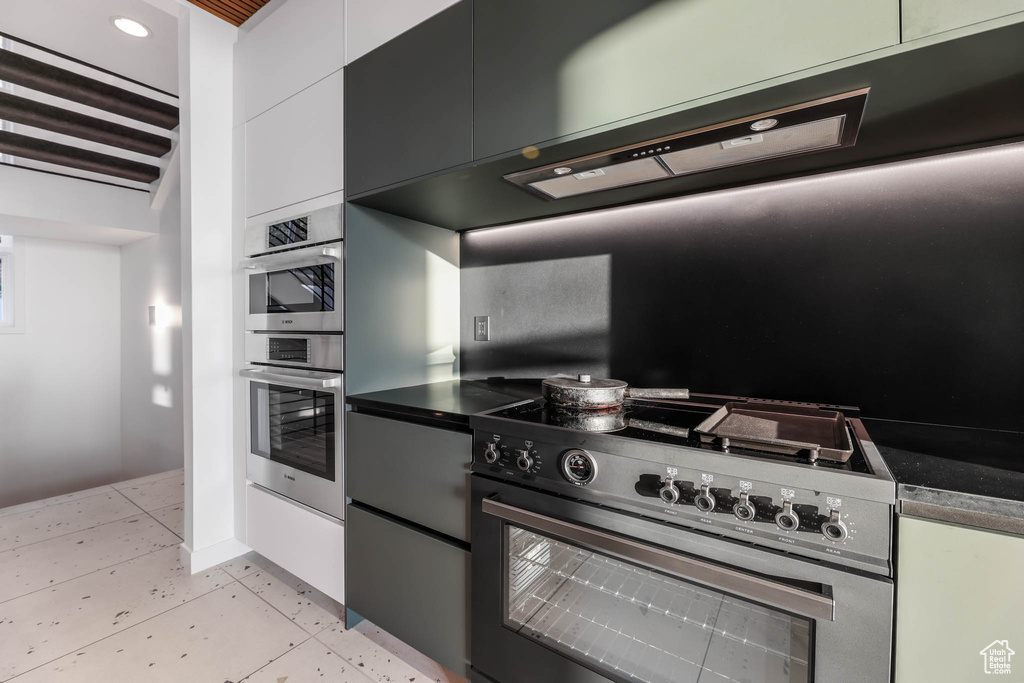 Kitchen with high end stove, dark countertops, ventilation hood, white cabinets, and recessed lighting