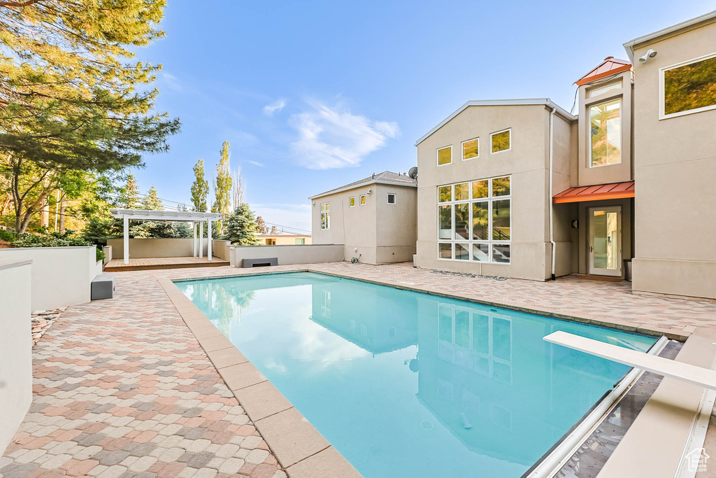 View of swimming pool featuring a patio, a pergola, and a diving board