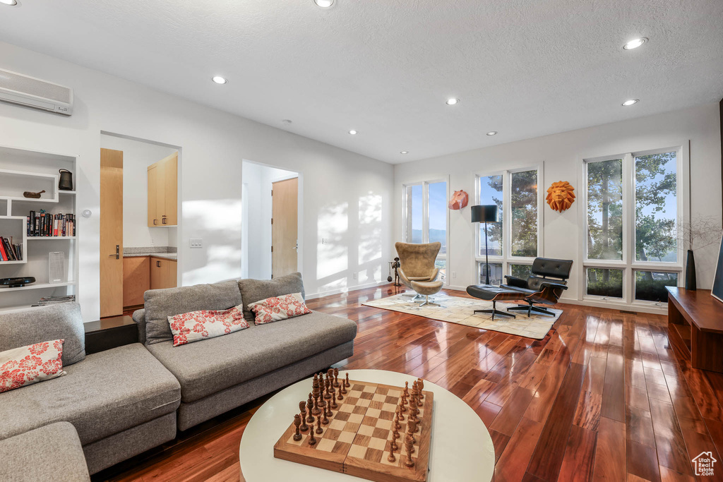 Living area with a wall mounted AC, wood-type flooring, recessed lighting, and a textured ceiling
