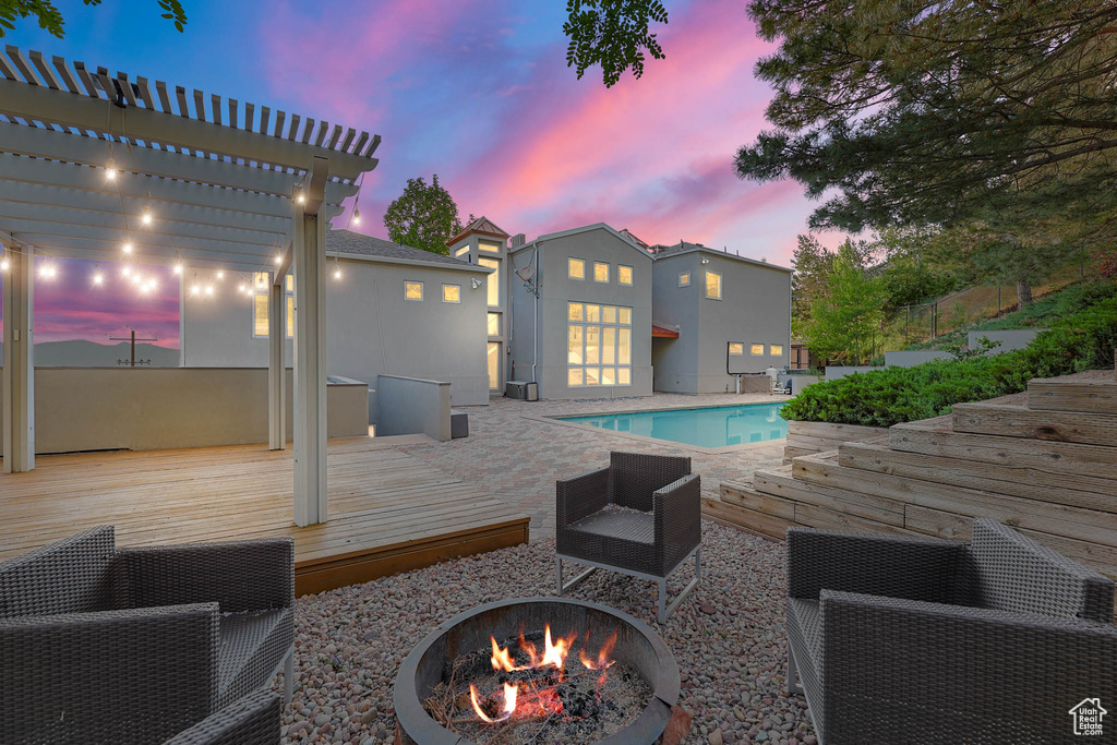 Pool at dusk with a fire pit, an outdoor pool, a deck, and a pergola